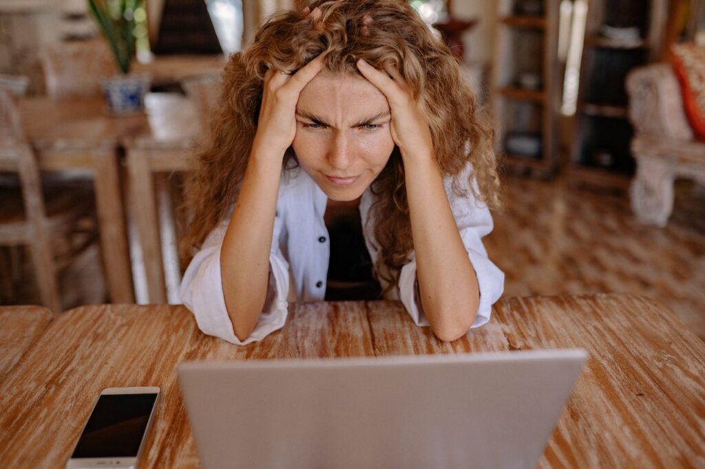 A woman holding her head in her hands looking at her computer worryingly.